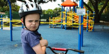 boy in blue denim vest and helmet riding red bicycle