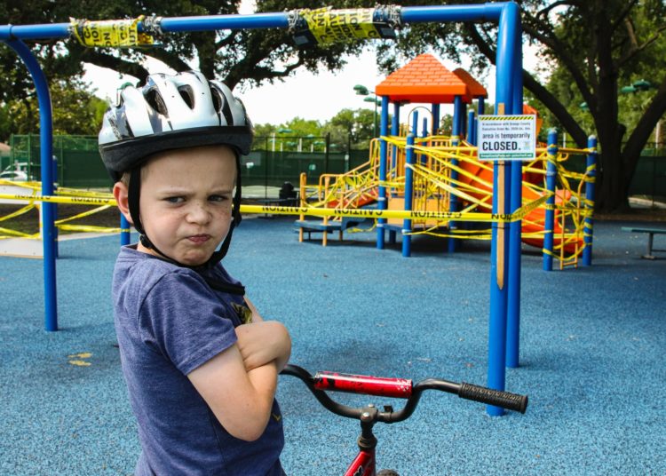 boy in blue denim vest and helmet riding red bicycle